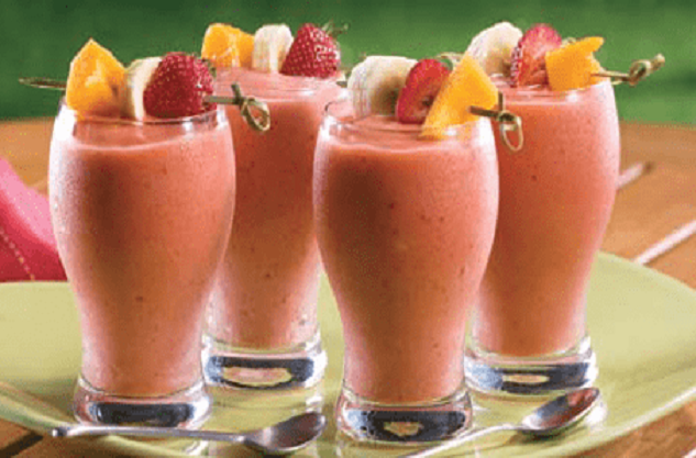 Four Pink smoothie in a glass topped with a slice of banana, mango, and strawberry