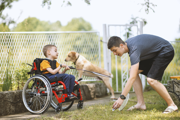 Young disabled child in wheelchair playing with dog and older brother
