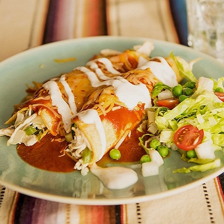 A white plate with two chicken enchiladas covered in enchilada sauce with a small side salad.
