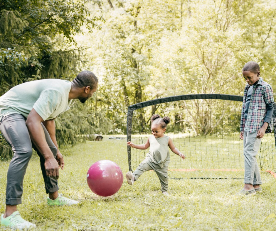 Father playing soccer outside with his son and daughter