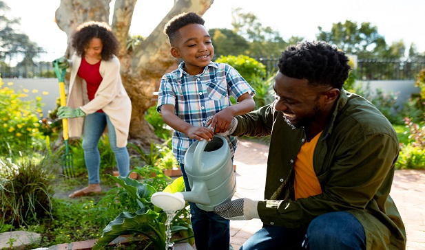 Young parents with son smiling and watering plants in a garden 